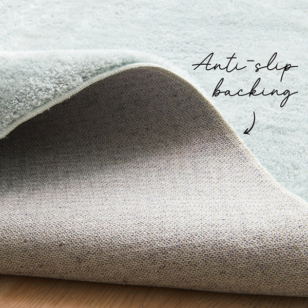 Pale blue soft rug corner showing plush texture and beige anti-slip backing on wooden floor.