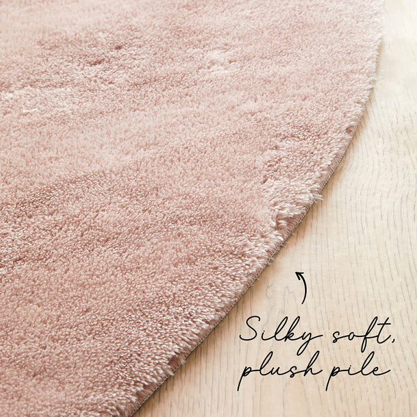 Round pale pink soft plush rug with dense pile on light wood floor.