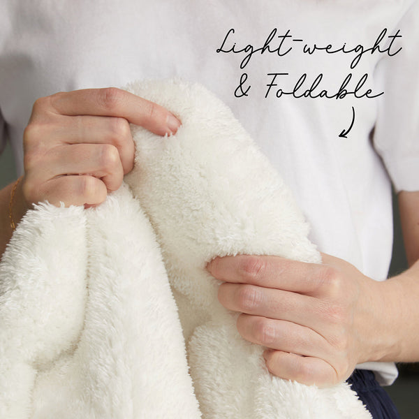 Hands holding a soft, fluffy white polyester rug showing its lightweight and foldable texture.