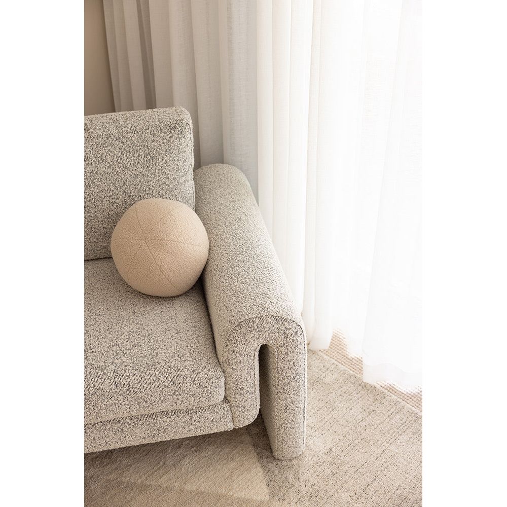 Gray textured sofa with a round beige pillow against a neutral background