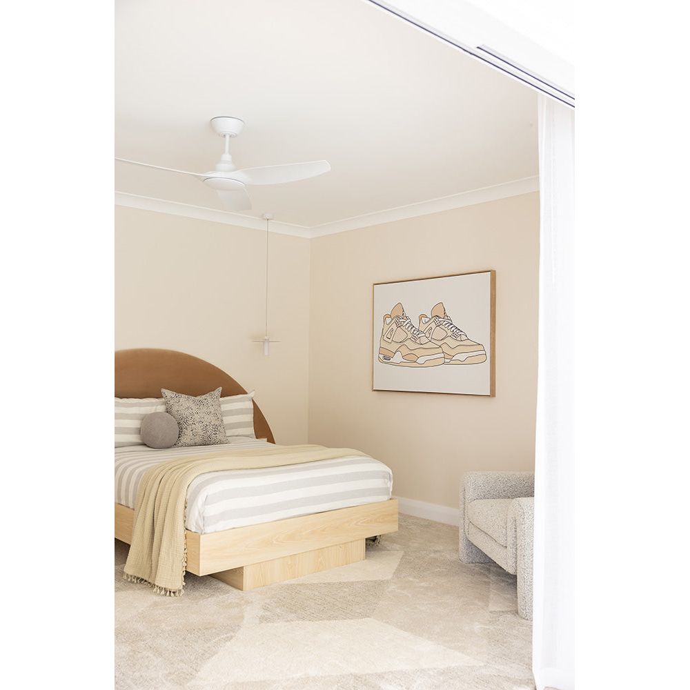 Modern bedroom with wooden bed, beige walls, and a framed picture of sneakers.