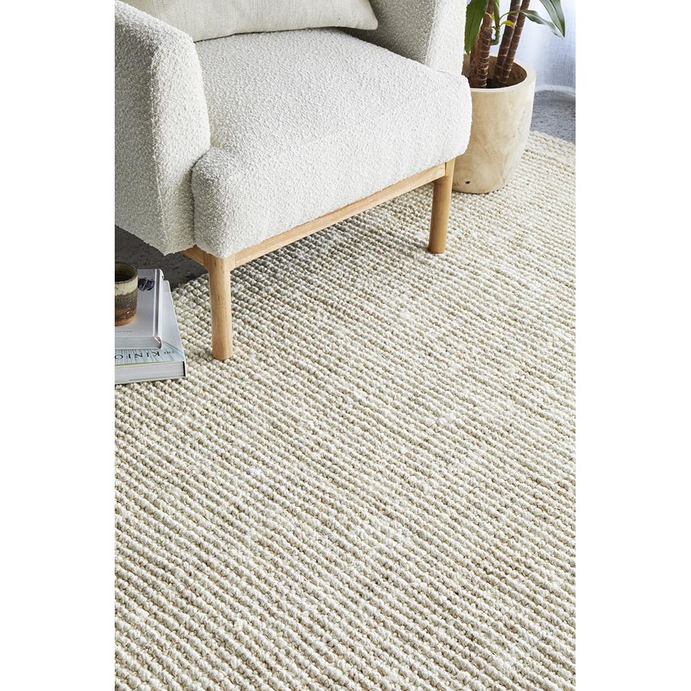 Beige textured rug with a chair and plant in the background