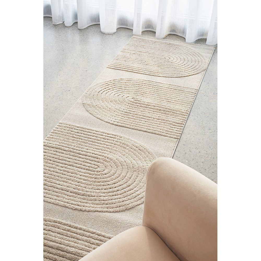 Beige runner rug with modern spiral and striped pattern on smooth floor near sheer curtains and beige chair.