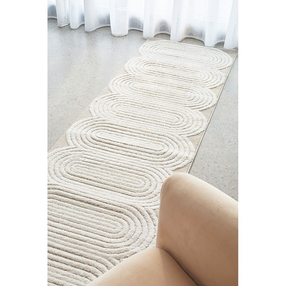 Beige and white runner rug with concentric oval patterns and scalloped edges on a light floor.
