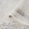 Beige rug with textured abstract pattern in muted blue and cream tones, soft woven fabric with subtle distressed effect.