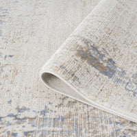 Beige rug with textured abstract pattern in muted blue and cream tones, soft woven fabric with subtle distressed effect.