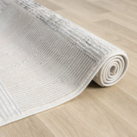 Beige and grey textured runner rug with subtle linear patterns, rolled on light wood floor.