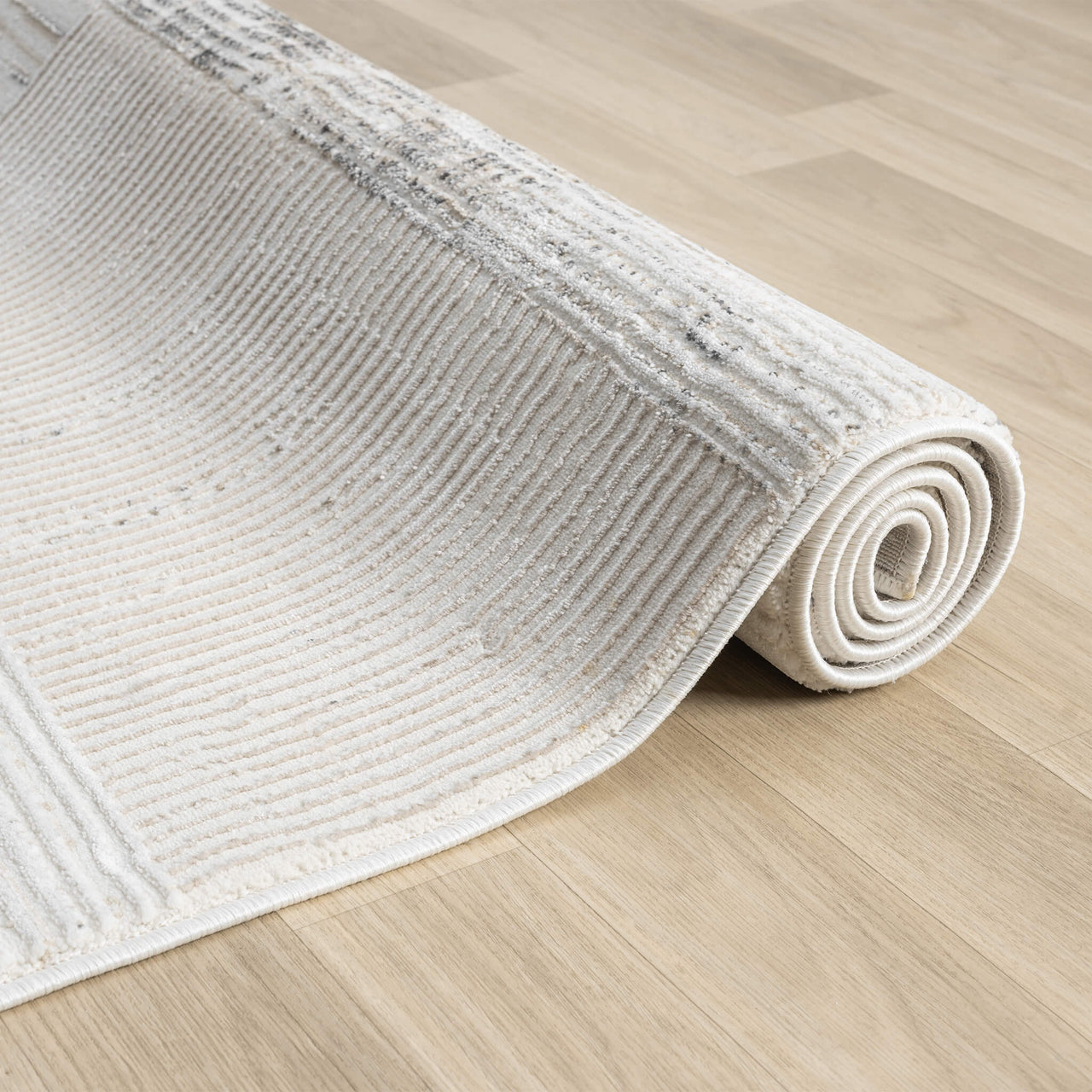 Beige and grey textured modern rug with subtle linear patterns rolled on wooden floor.