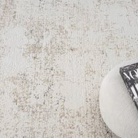 Beige and grey modern rug with subtle textured pattern and soft finish, next to round beige cushion with black and white book.