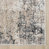 Beige and grey modern area rug with abstract textured pattern and white edge trim on hardwood floor.