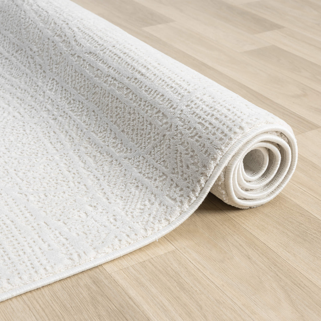 Cream-colored modern rug with subtle textured geometric pattern, partially rolled on light wood floor.