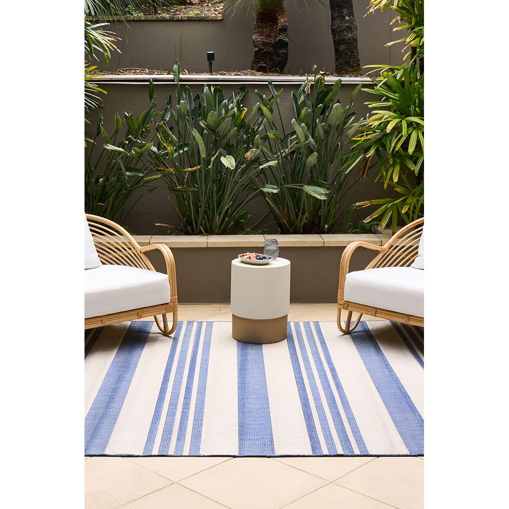 Outdoor seating area with two wicker chairs and a small table on a blue and white striped rug.
