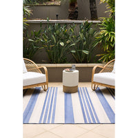 Outdoor seating area with two wicker chairs and a small table on a blue and white striped rug.