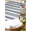 Striped blue and white rug with a wicker chair and white ottoman on a tiled floor.