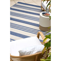 Striped blue and white rug with a wicker chair and white ottoman on a tiled floor.