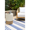 Outdoor setting with a white and brown side table, wicker chair, and striped rug.