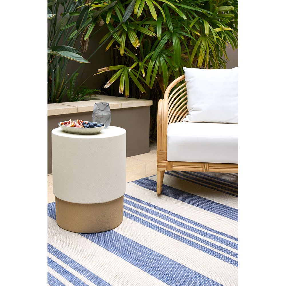 Outdoor setting with a white and brown side table, wicker chair, and striped rug.