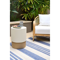 Outdoor setting with a white and brown side table, wicker chair, and striped rug.
