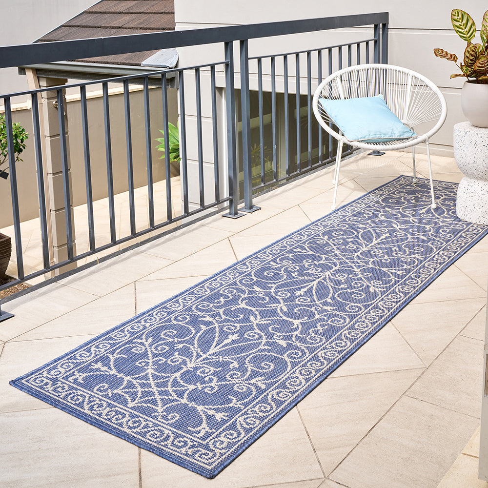 Blue patterned outdoor runner rug on a patio with a chair and plants.