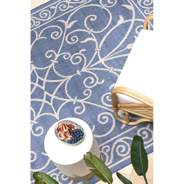 Blue indoor-outdoor rug with modern white swirling geometric pattern, flat-weave texture.