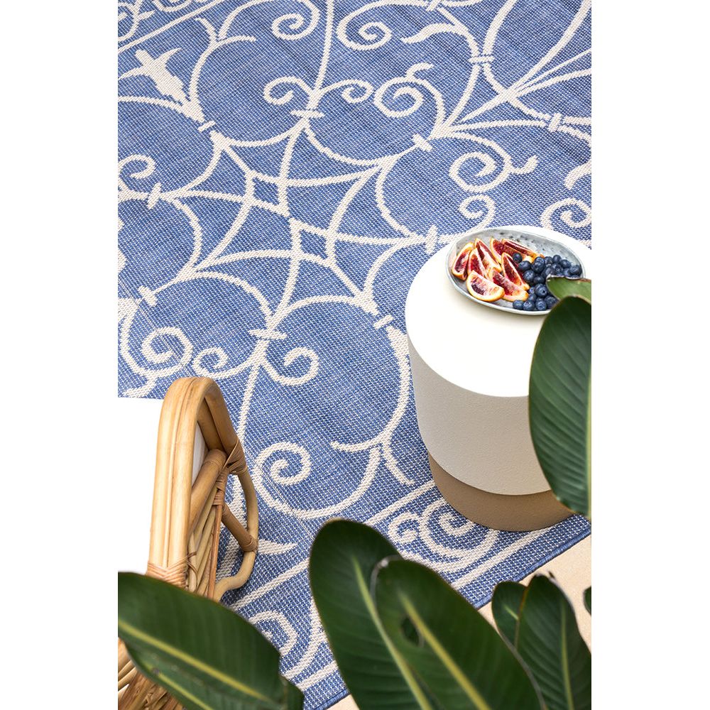 Blue patterned rug with a white stool and fruit bowl on a tiled floor.