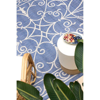 Blue patterned rug with a white stool and fruit bowl on a tiled floor.