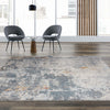 Grey multi-colored abstract patterned rug with subtle blue and orange accents on wood floor.