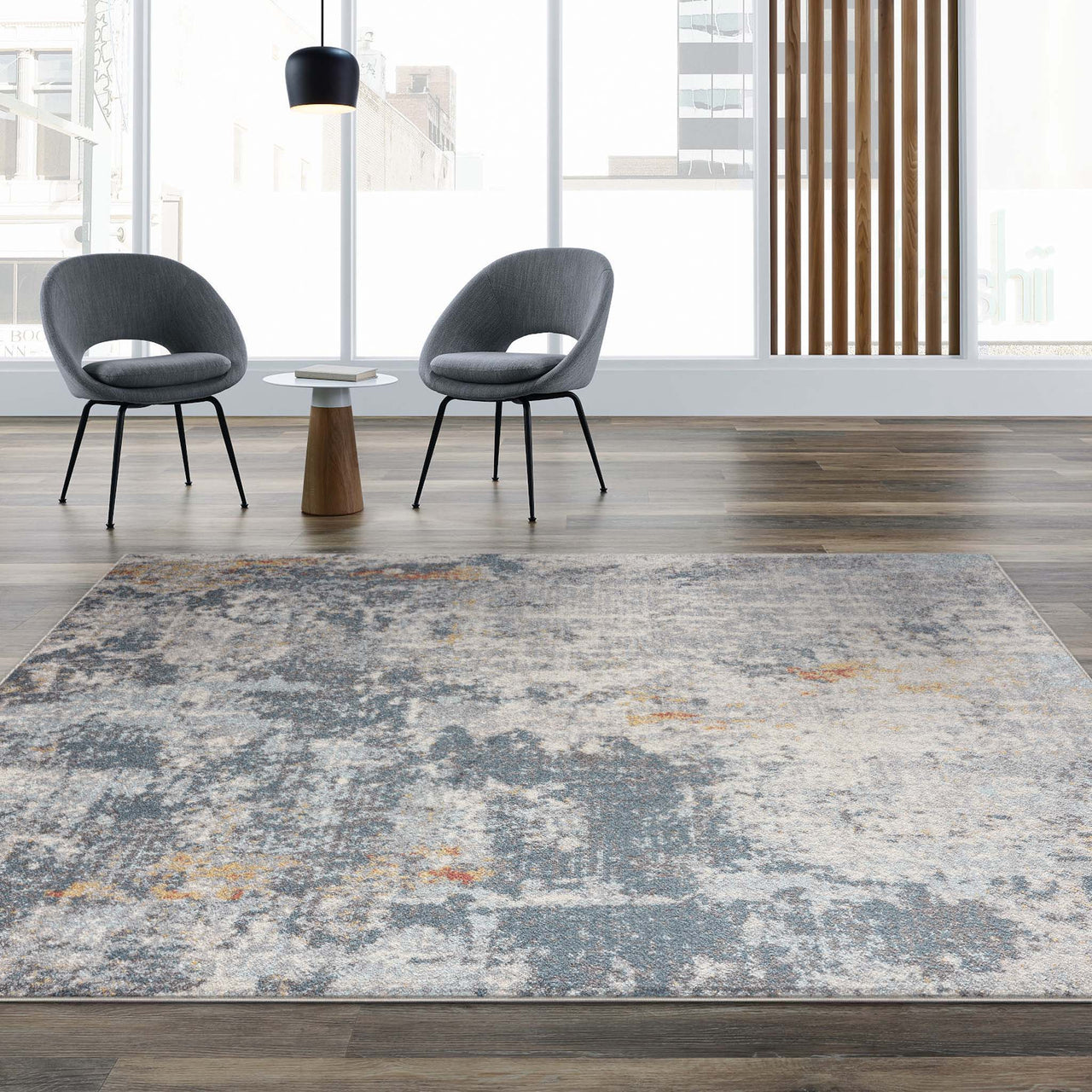 Grey multi-colored abstract patterned rug with subtle blue and orange accents on wood floor.