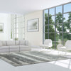 Grey, white, and blue abstract patterned modern rug with fringed edges in a bright, minimalist living room.