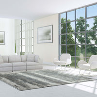 Grey, white, and blue abstract patterned modern rug with fringed edges in a bright, minimalist living room.