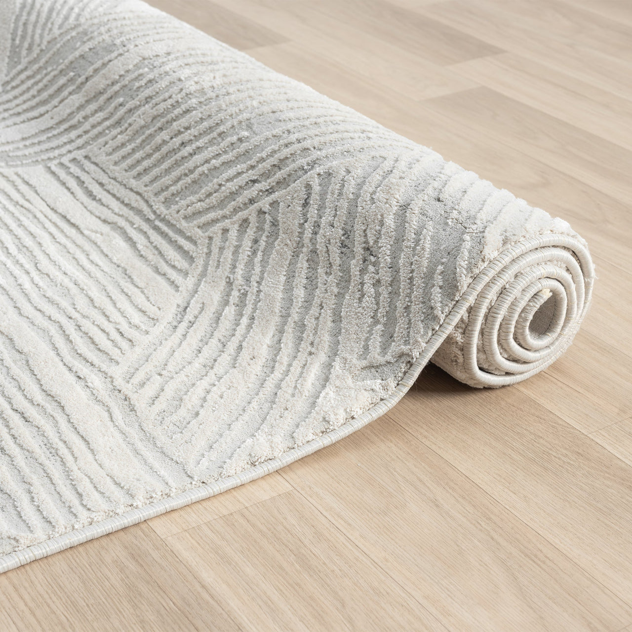 Light grey modern rug with textured geometric pattern on wooden floor, rolled edge visible.