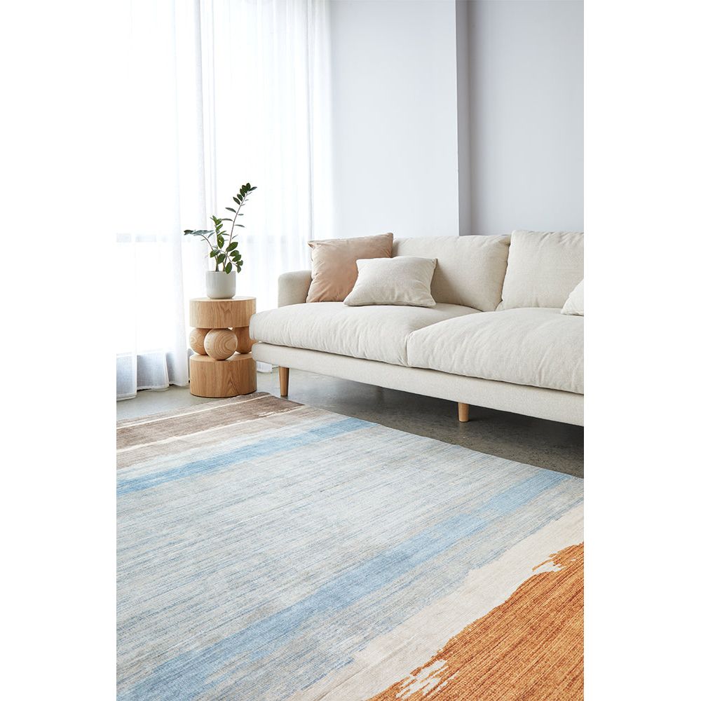 Multicoloured modern rug with blue, beige, and rust stripes on hardwood floor under cream sofa.