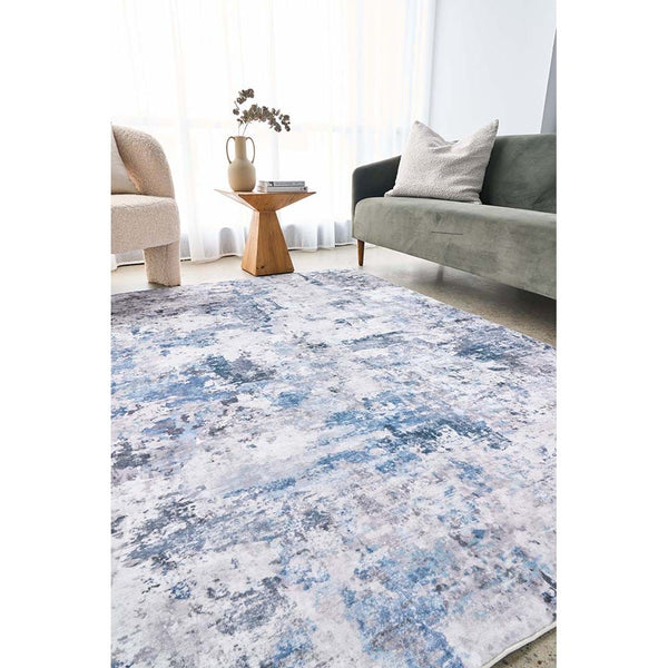 Blue and gray abstract patterned modern rug on light hardwood floor in living room setting.