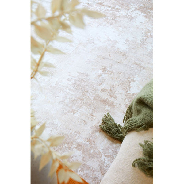 Neutral-toned modern rug with subtle abstract pattern, plush texture, next to a green fringed throw blanket.
