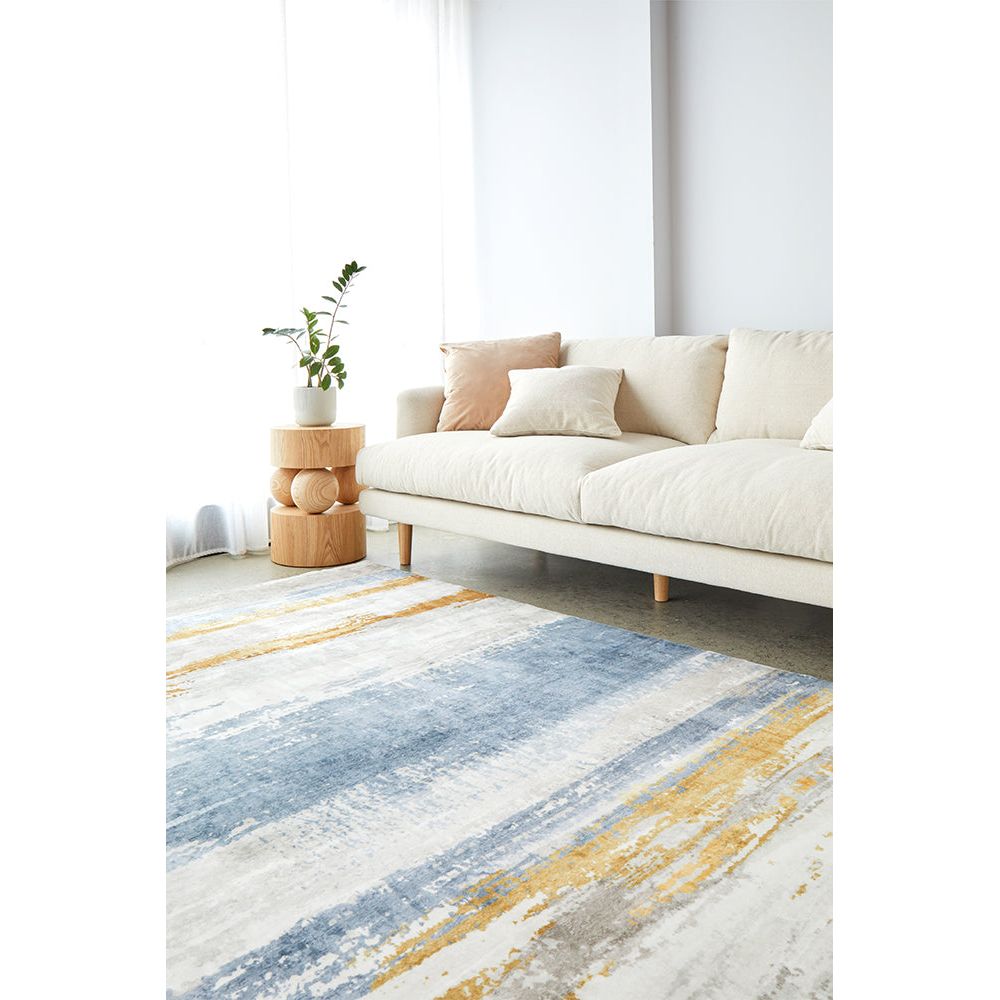 Blue, grey, and mustard abstract modern rug with a washed texture under a beige sofa.