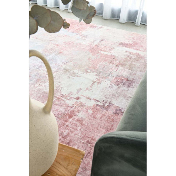 Pastel pink abstract rug with soft textured patterns on hardwood floor near modern furniture.