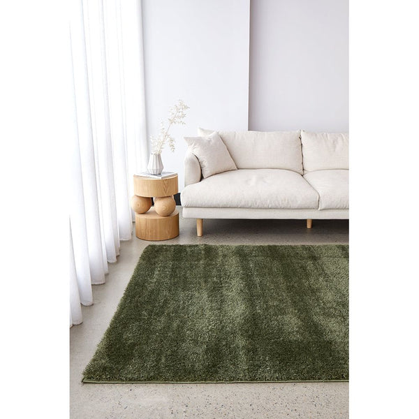 Green modern soft shaggy rug with thick polyester pile on light floor near beige sofa.
