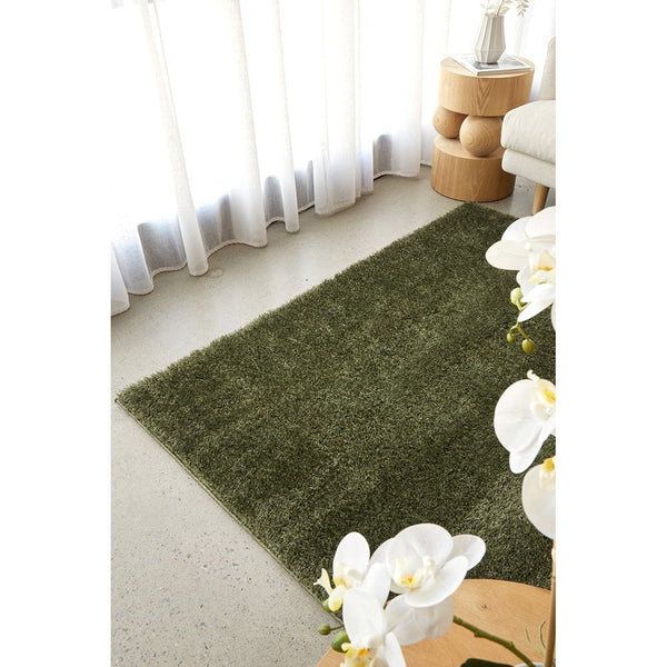 Rectangular deep green soft shaggy rug on light-colored floor with natural light filtering through sheer curtains.