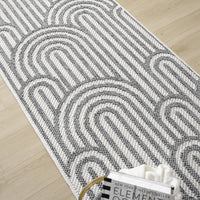 Grey flatweave runner rug with minimalist geometric arch pattern on light wood floor.