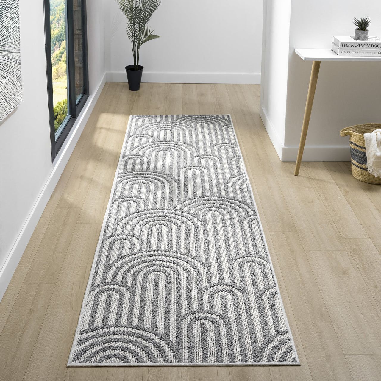 Grey flatweave runner rug with repeating arch geometric pattern in light and dark tones on light wood floor.