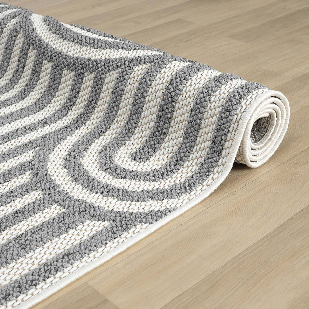 Rolled grey and white flatweave runner rug with curved geometric stripes on light wood floor.