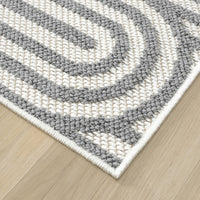 Corner close-up of Wiluna 4658 grey geometric flatweave rug with arch pattern on light wood floor.