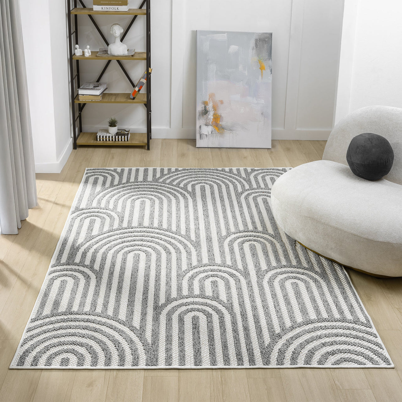 Grey flatweave rug with overlapping geometric arch patterns in white and dark grey tones on hardwood floor.