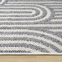 Grey flatweave rug with textured geometric arch pattern on a wooden floor.