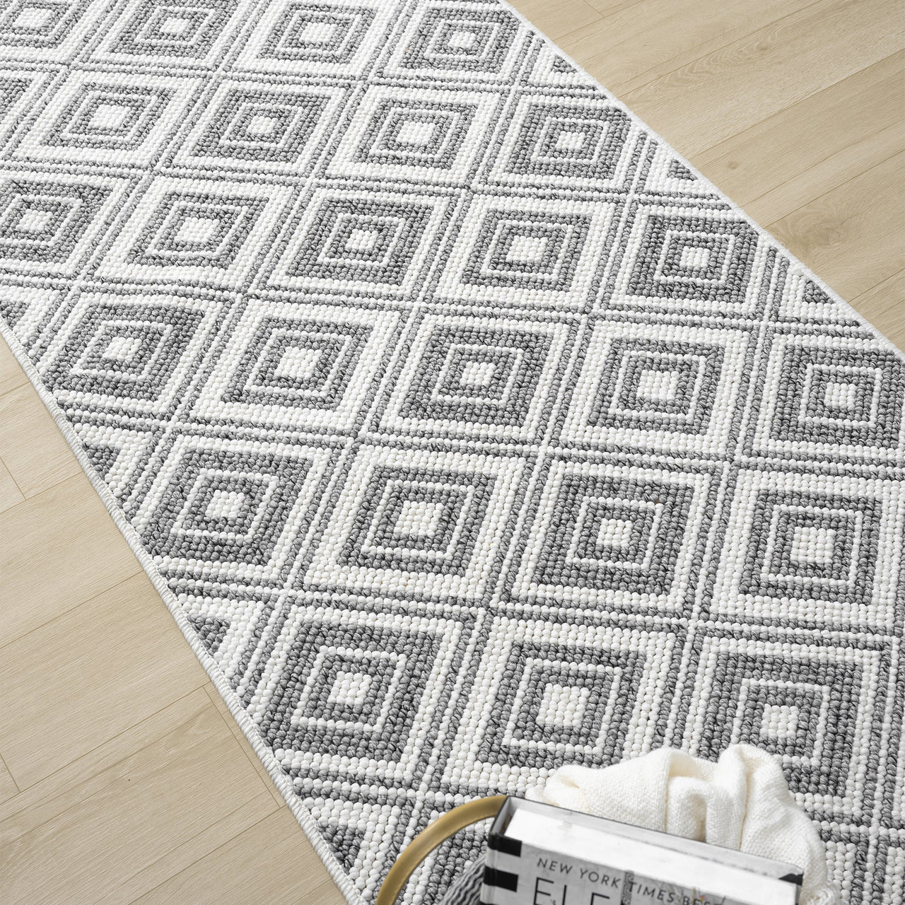 Grey flatweave runner rug with repeating geometric diamond pattern on light wood floor.