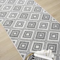 Grey flatweave runner rug with repeating geometric diamond pattern on light wood floor.