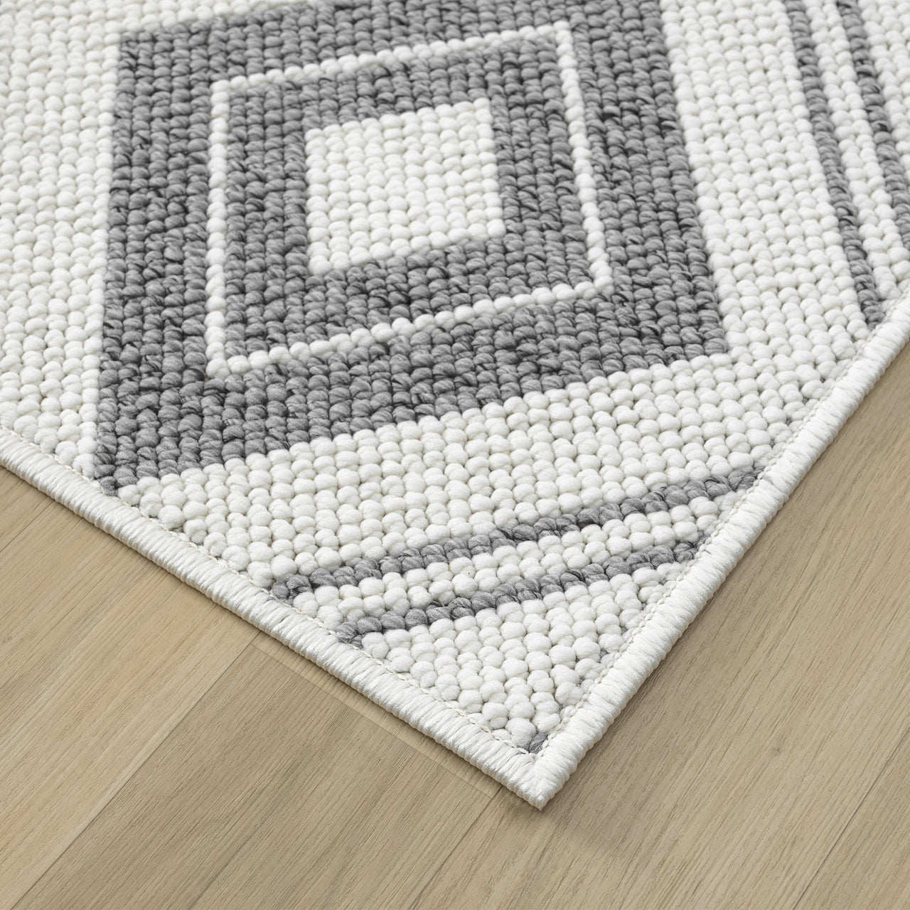 Corner of grey and white geometric flatweave runner rug with textured square pattern on light wood floor.