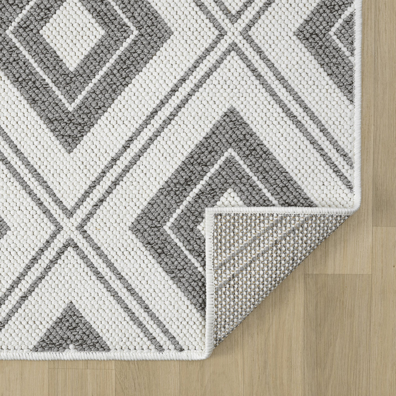 Grey flatweave runner rug with monochrome geometric diamond pattern on wood floor.