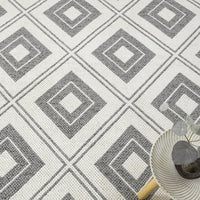 Grey flatweave rug with a repeating geometric diamond pattern in shades of grey and white.