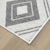 Grey and white flatweave rug corner with geometric diamond pattern on wood floor.